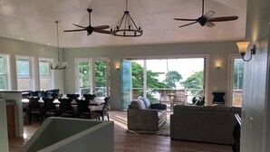 Un vaste espace de vie comprenant une table à manger, plusieurs canapés, des ventilateurs de plafond et de grandes fenêtres offrant une vue sur l’extérieur.