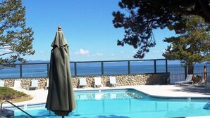 Una piscina con un muro de piedra y sillas de descanso, con vista a una extensión de agua.