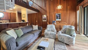 A spacious living area with a wooden ceiling, a gray sofa, patterned armchairs, a wooden coffee table, and a dining table with chairs. - Kingwood Condo | Community Pool & Tennis Courts (Kings Beach)