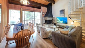 A wooden interior with a stone fireplace, a dining table with chairs, a sofa, and a TV. - Kingwood Condo | Community Pool & Tennis Courts (Kings Beach)