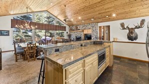 A spacious kitchen with a large island, wooden ceiling, stone accents, and a mounted moose head.