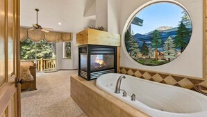 A bathroom with a large bathtub, a fireplace, and a circular stained glass window.