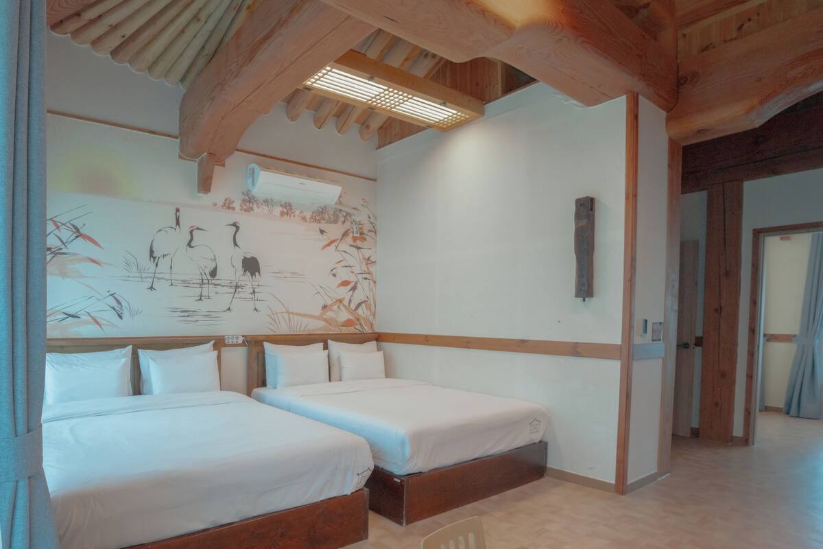 Een hotelkamer met twee bedden, een houten plafond, een muurschildering en een houten tafel.