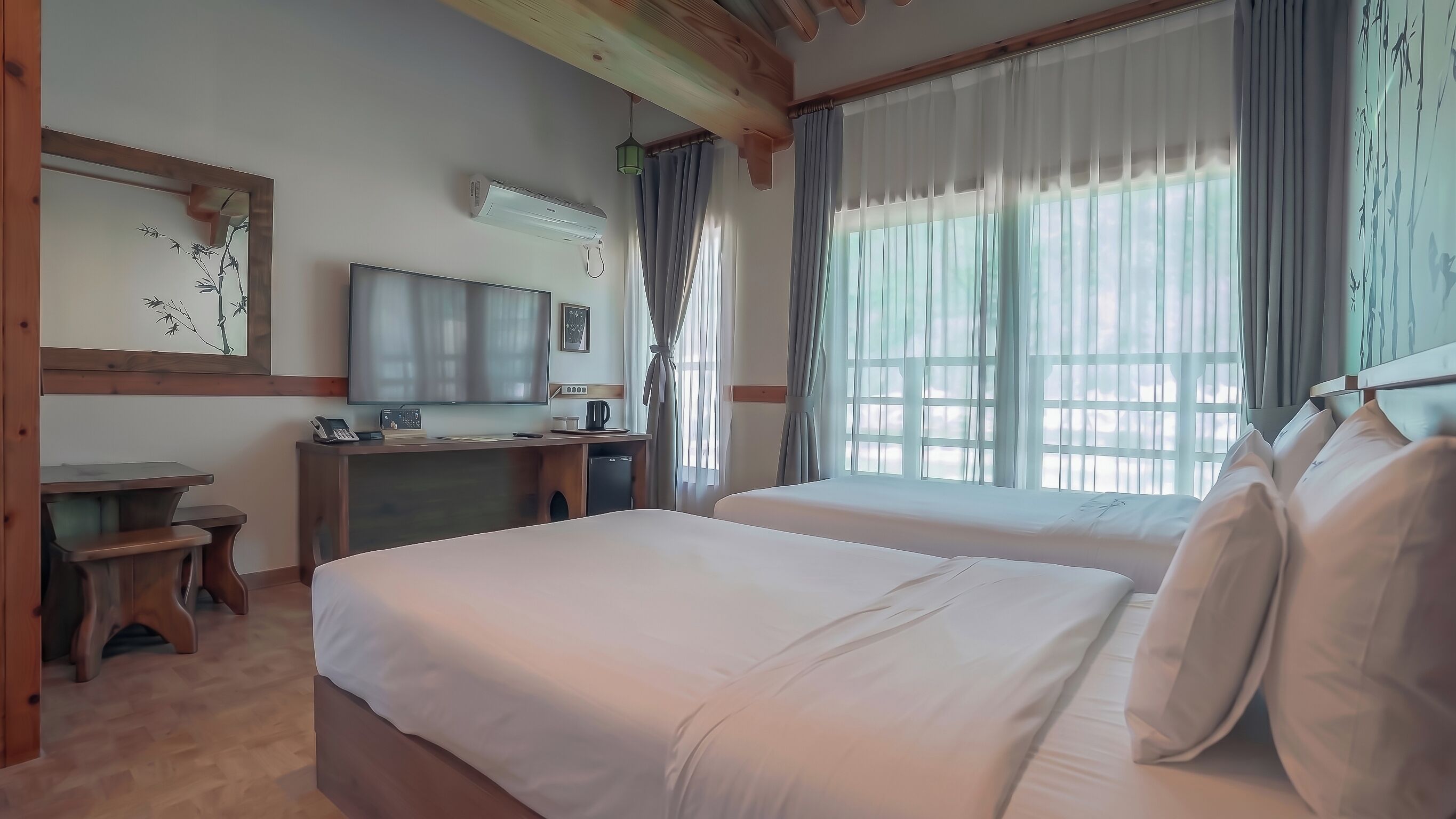 A hotel room with two beds, a desk with a telephone, a flat-screen TV, and a window with curtains.