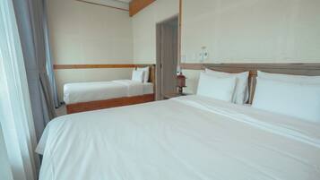 A hotel room with two single beds, a wooden headboard, a nightstand with a lamp, and a door leading to another room.