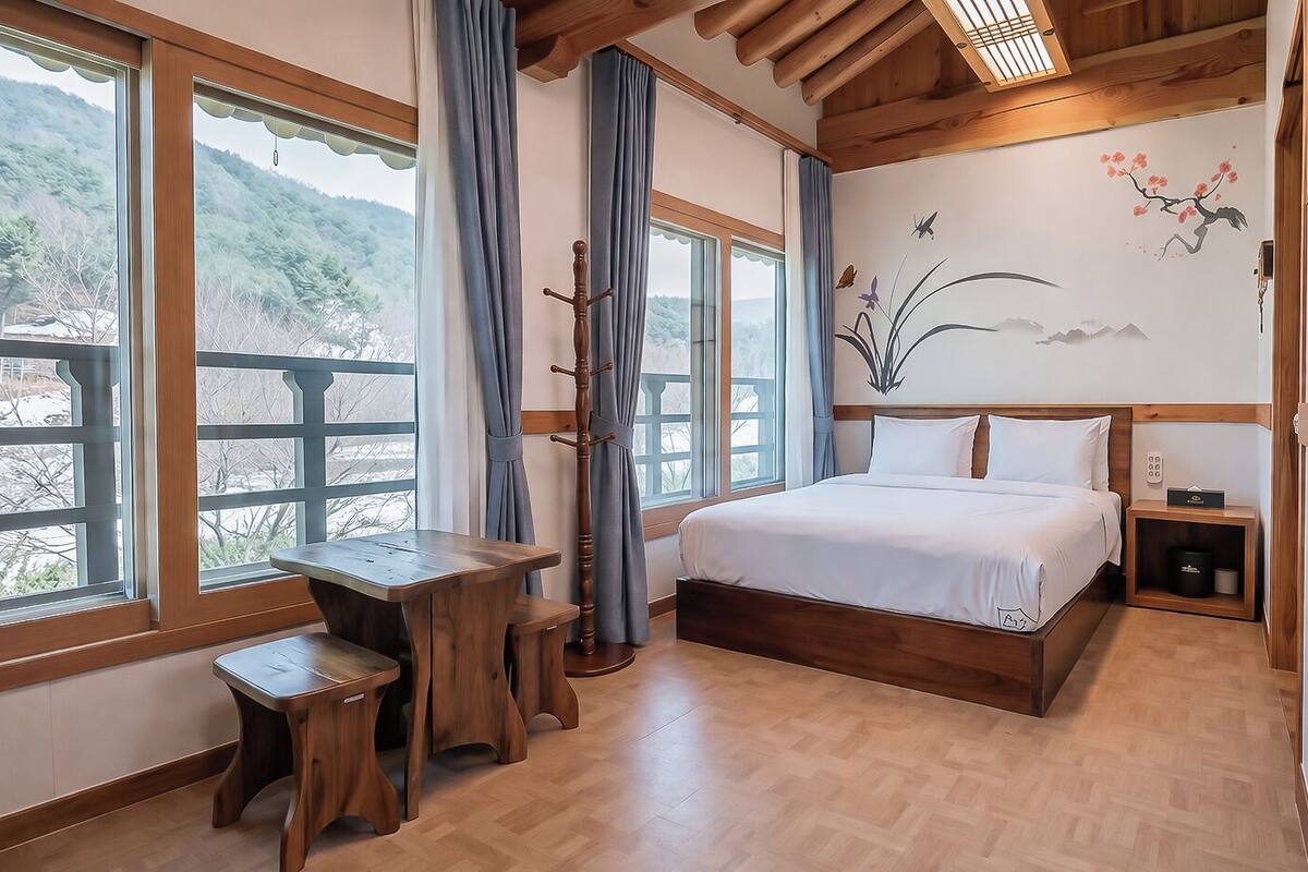 Een slaapkamer met een houten bed, een bureau en uitzicht op een bergachtig landschap door grote ramen.