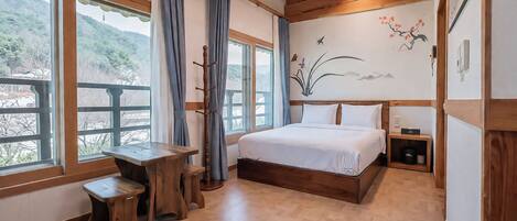 A bedroom with a wooden bed, a desk, and a view of a mountainous landscape through large windows.