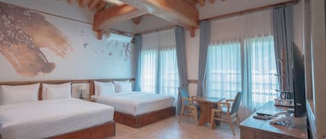 Quarto de hotel com duas camas, uma mesa de trabalho com cadeira, televisão e janelas amplas com cortinas.