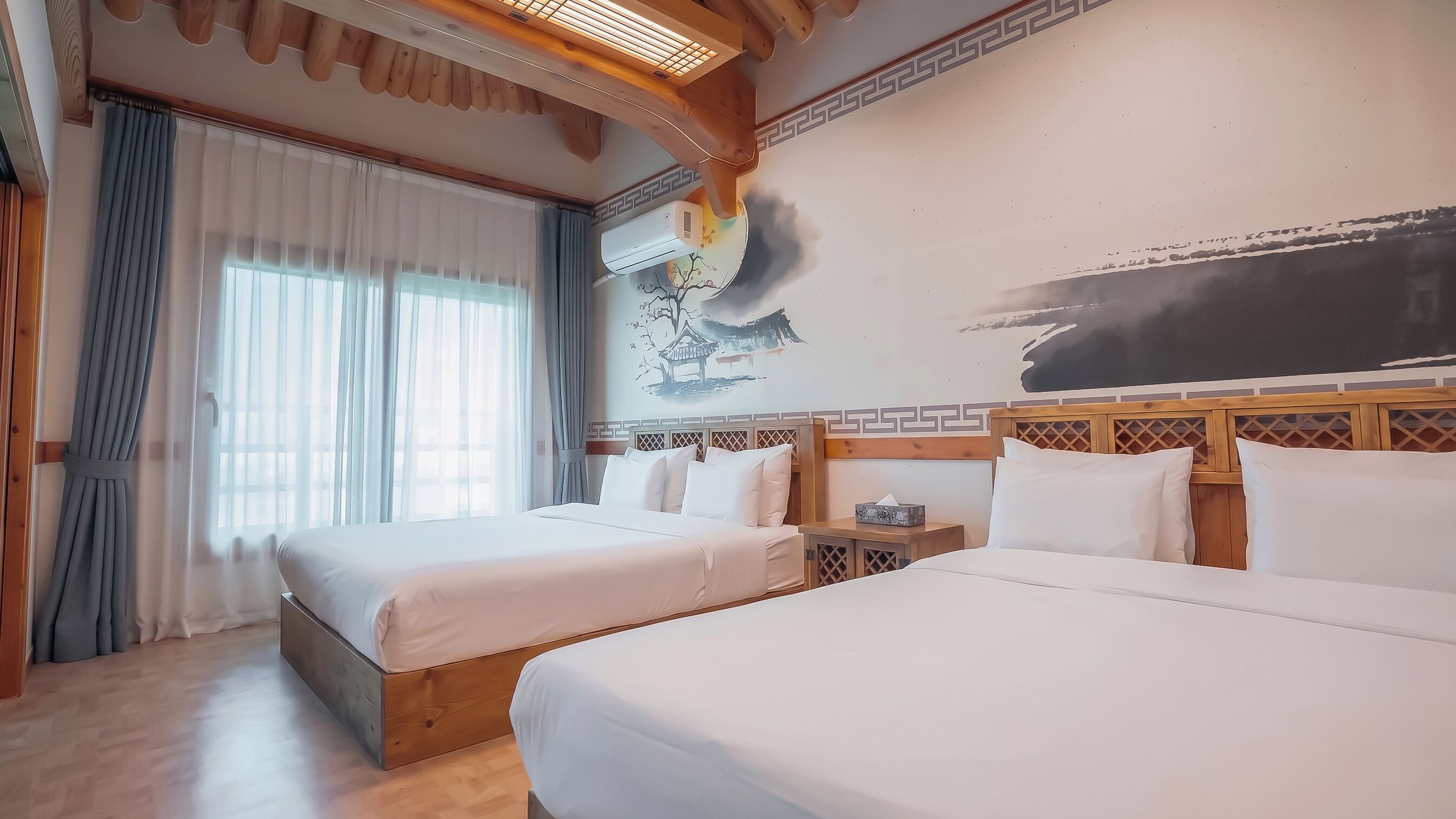 Une chambre d’hôtel avec deux lits, une grande fenêtre avec des rideaux, un climatiseur fixé au mur et un tableau de style traditionnel.