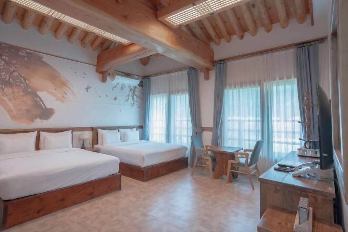 Een hotelkamer met twee bedden, een bureau, een stoel en een groot raam met gordijnen.