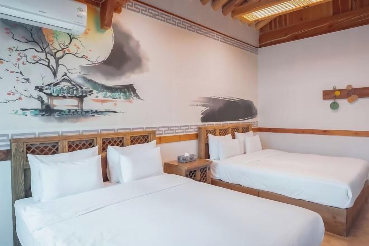 A room with two beds, a wooden headboard, a wall painting, and a wooden ceiling.