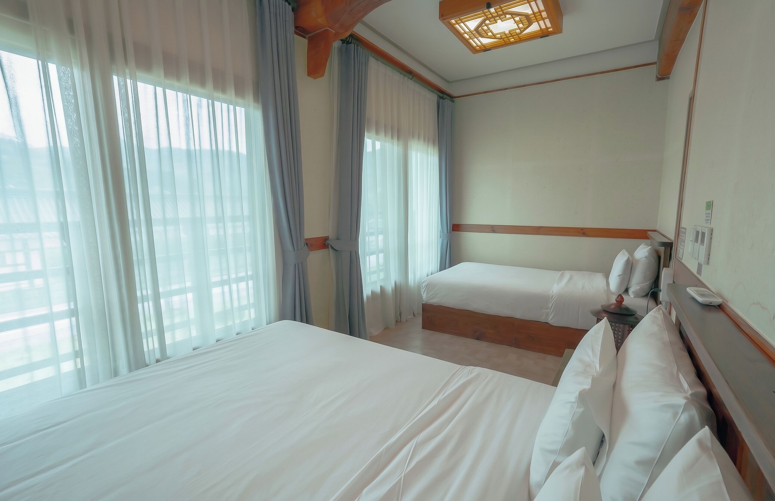 A hotel room with two beds, a wooden headboard, a bedside table, and a window with curtains.