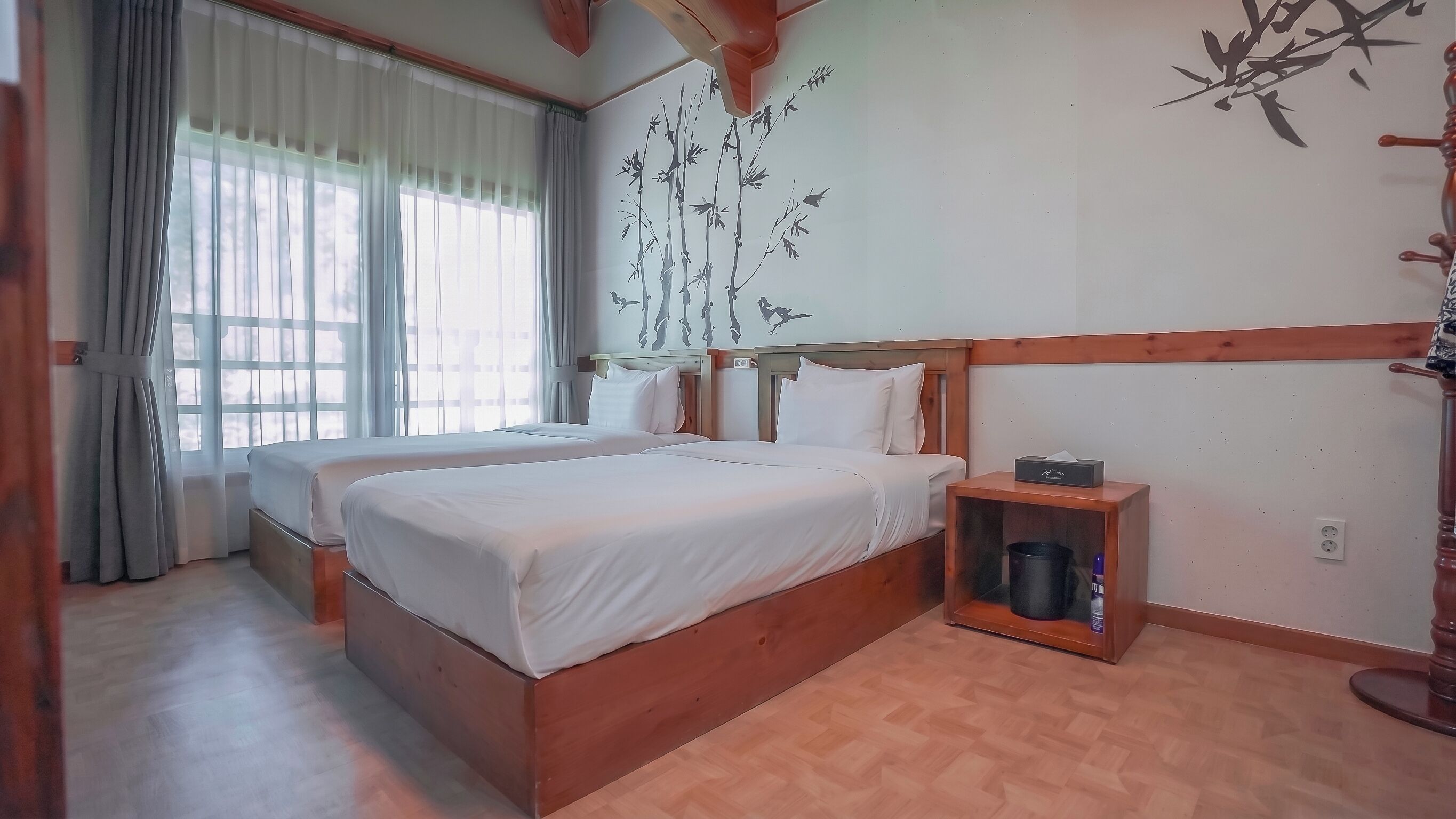 A bedroom with two beds, a wooden headboard, a nightstand, and a wall with a bamboo and bird mural.