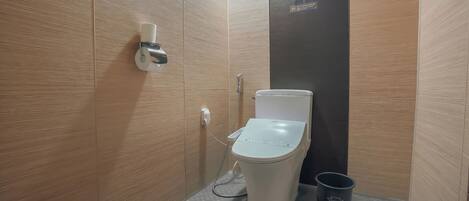 Une salle de bain moderne équipée de toilettes, d’un distributeur d’essuie-tout, d’une douche et d’une poubelle.