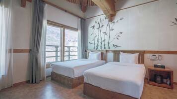 A hotel room with two beds, a wooden headboard, a window with curtains, a wall-mounted phone, and a bedside table with a tissue box.