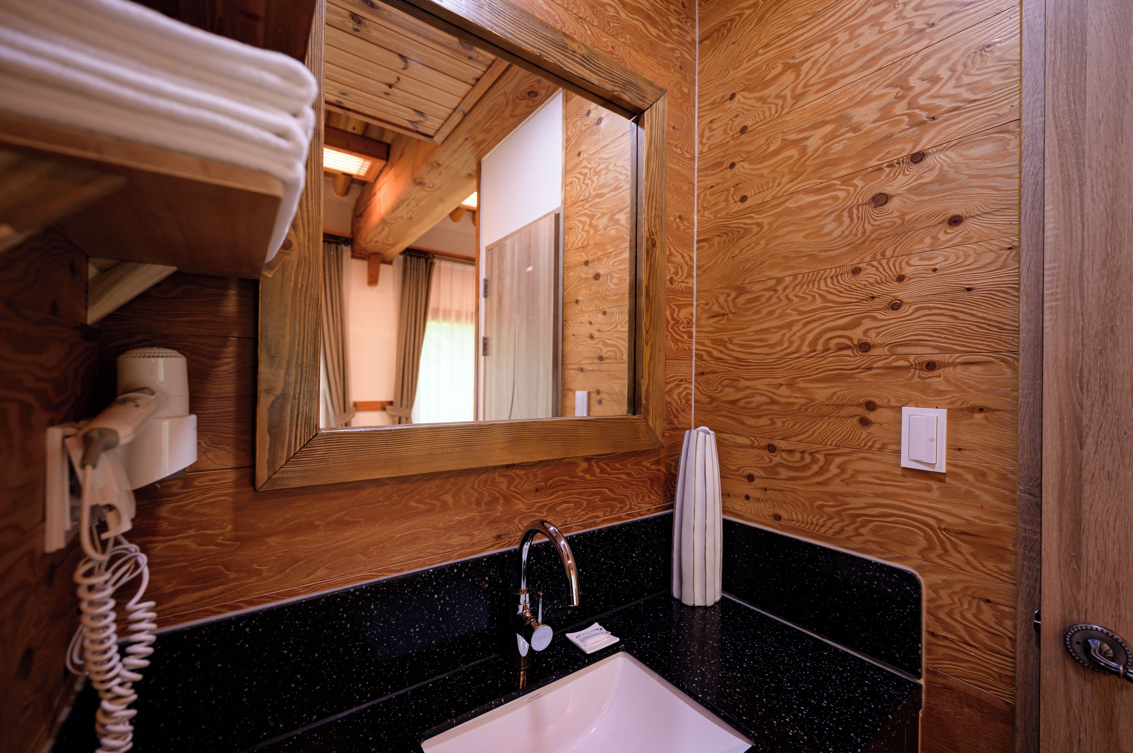 Un interior de madera con un lavabo de encimera negra, un espejo, un perchero para toallas y un teléfono.