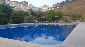 Una piscina con borde de azulejos, rodeada de sillas de descanso y follaje.