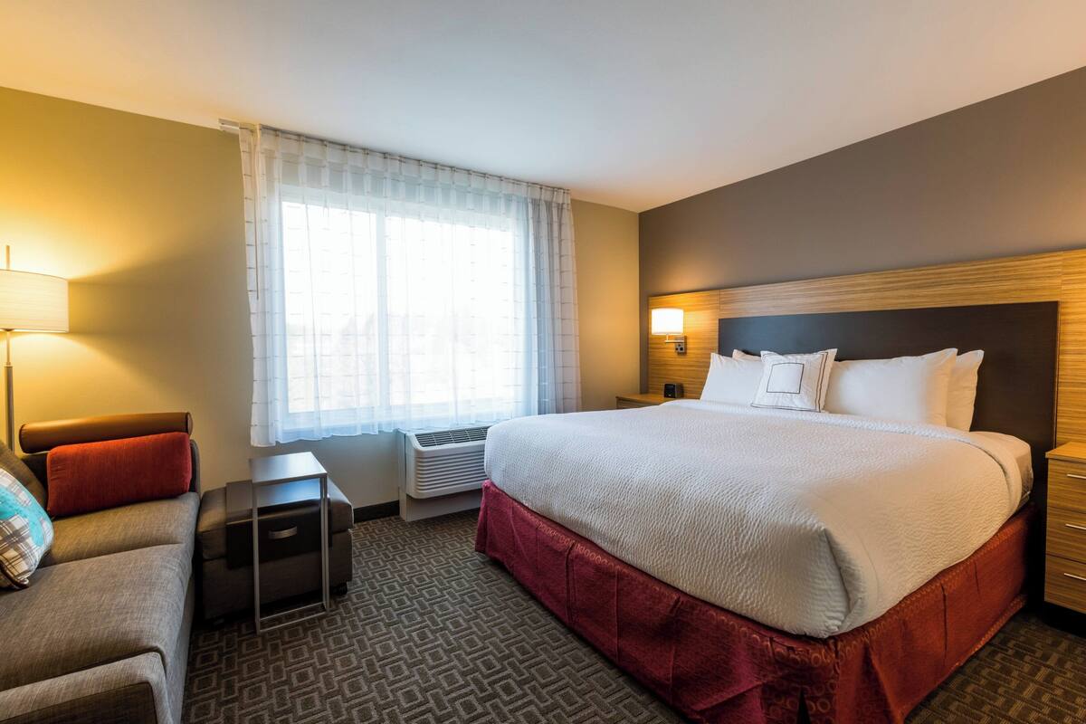 A hotel room with a large bed, a desk, a chair, a lamp, and a window with curtains.