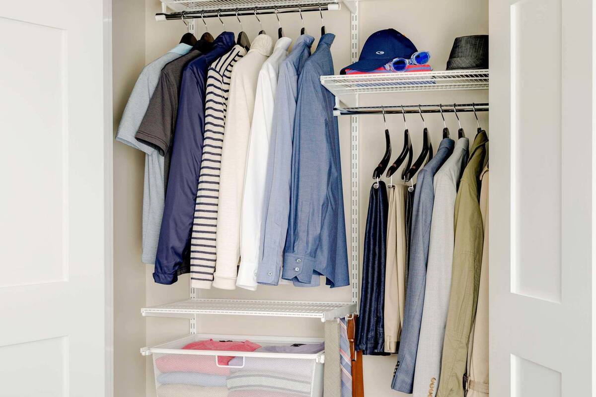 A walk-in closet with hanging clothes, shelves with folded clothes, and a suitcase.
