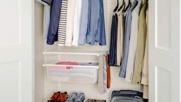 A walk-in closet with hanging clothes, shelves with folded clothes, and a suitcase.