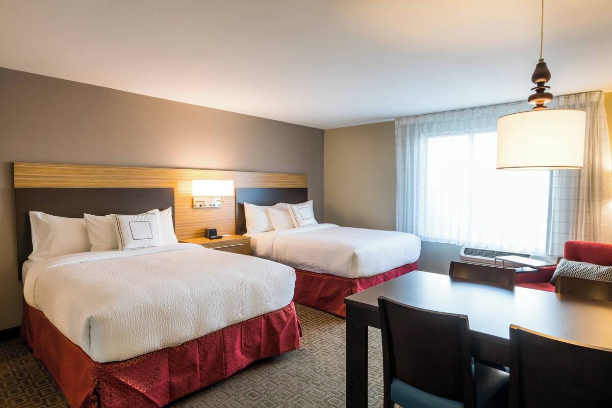 A hotel room with two beds, a desk, and a chair.
