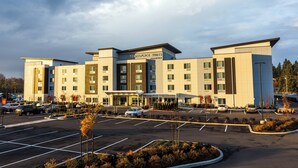 A multi-story hotel with a central entrance, parking lot, and a sign reading "TownePlace Suites."