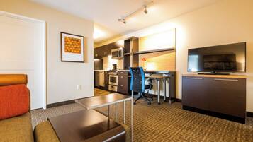 Quarto de hotel com sofá, escrivaninha, cadeira, televisão, micro-ondas e cozinha.