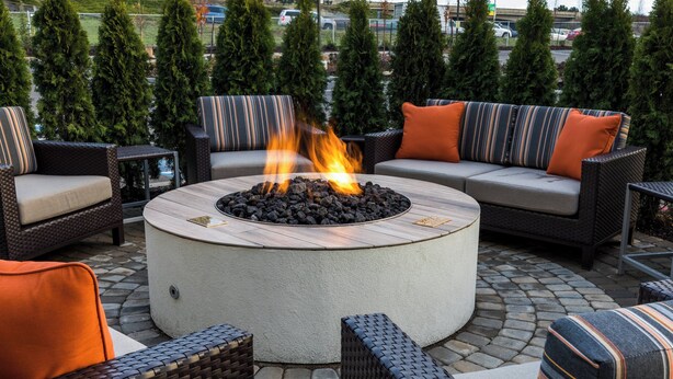 A circular fire pit surrounded by wicker furniture and a sofa with striped cushions.