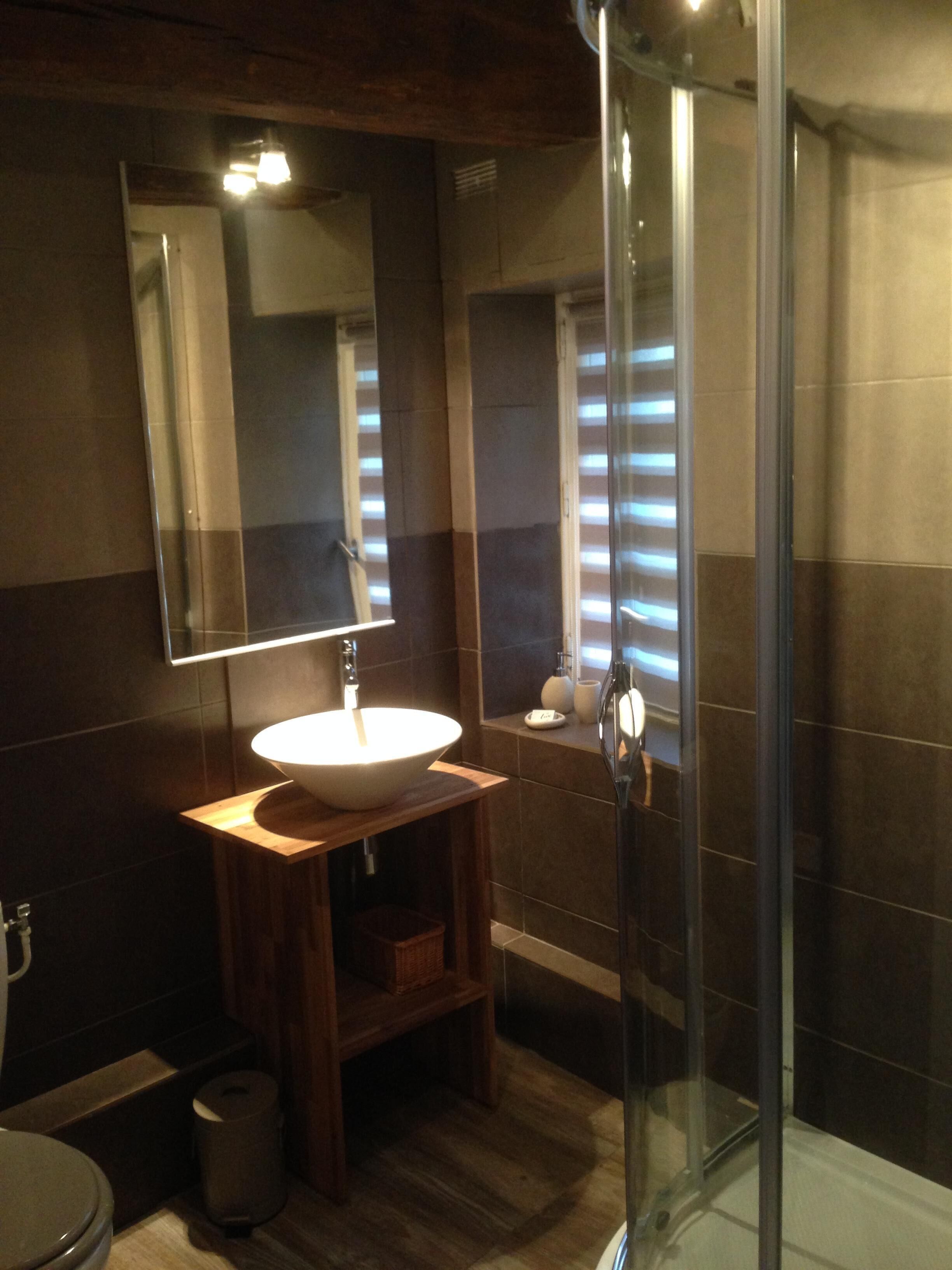 Un baño con tocador de madera, lavamanos blanco, espejo y cabina de ducha de vidrio.