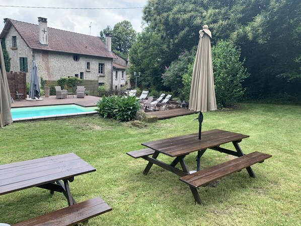 A backyard with a swimming pool, picnic tables, lounge chairs, and a covered umbrella.