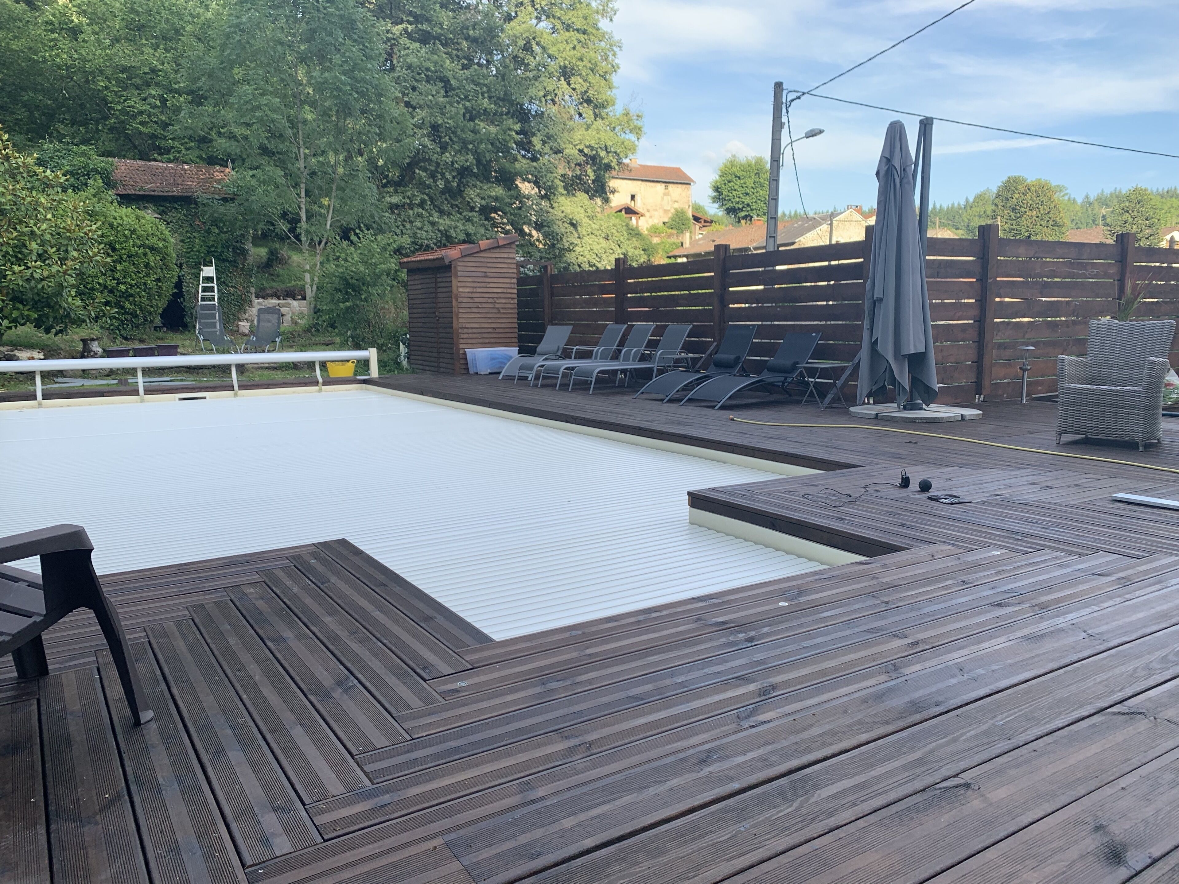 A wooden deck with a swimming pool, lounge chairs, and a wooden fence.