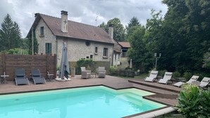 Une piscine avec des chaises longues et, au fond, une maison en pierre.