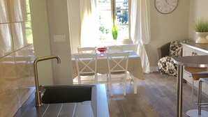Une cuisine moderne avec un évier encastré, des chaises blanches, une table à manger et une horloge au mur.