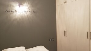 Een slaapkamer met een bed, twee kussens, een kledingkast en een wand met een lamp.