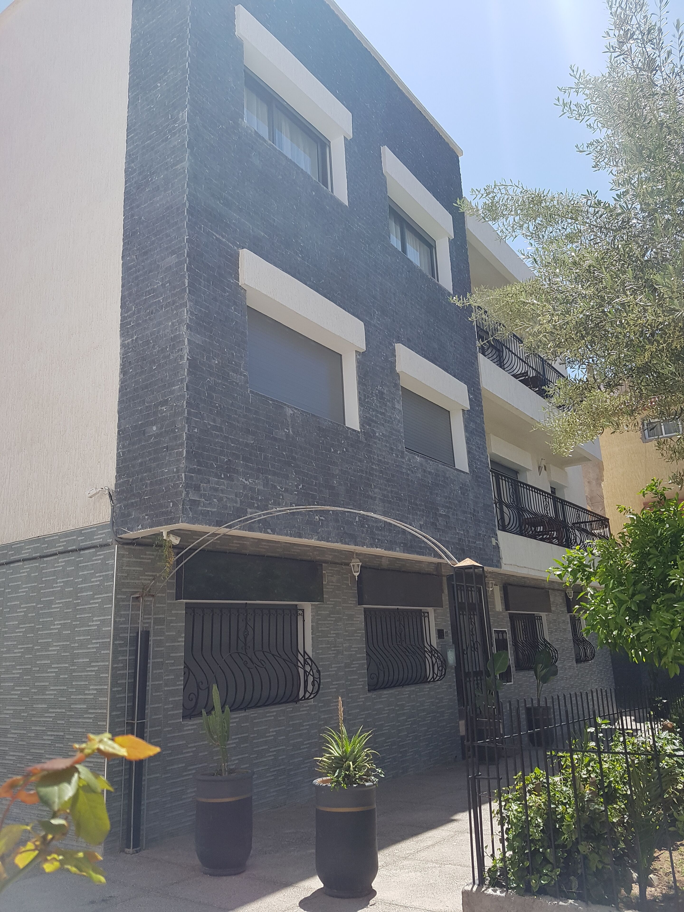 Un edificio de varios pisos con fachada oscura, ventanas grandes y un balcón con barandillas negras.