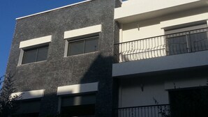 Een modern gebouw met een donkere gevel, grote ramen en een balkon met decoratieve metalen hekwerk.