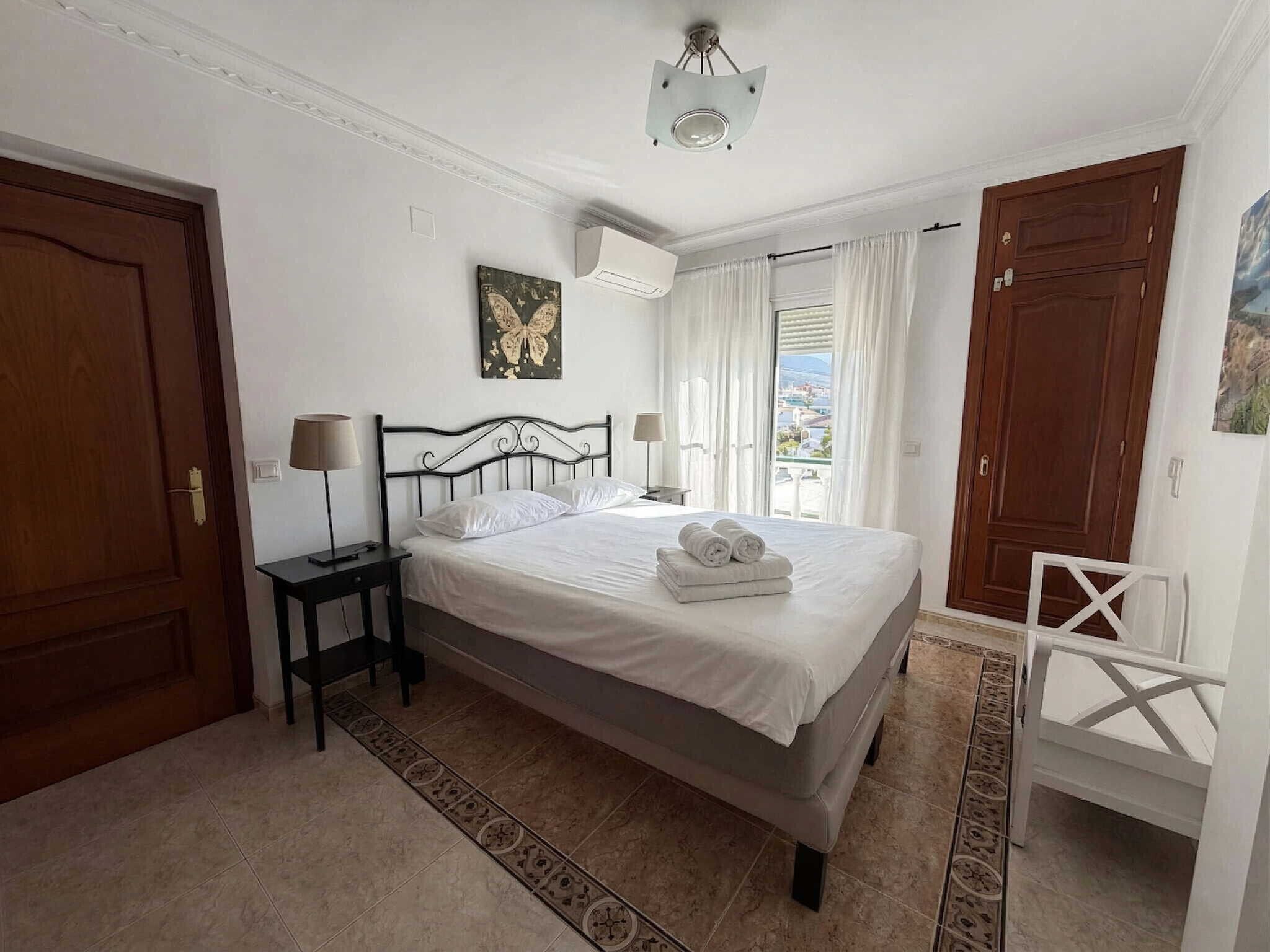 A bedroom with a bed, bedside tables, a lamp, a painting, and a view through the window.