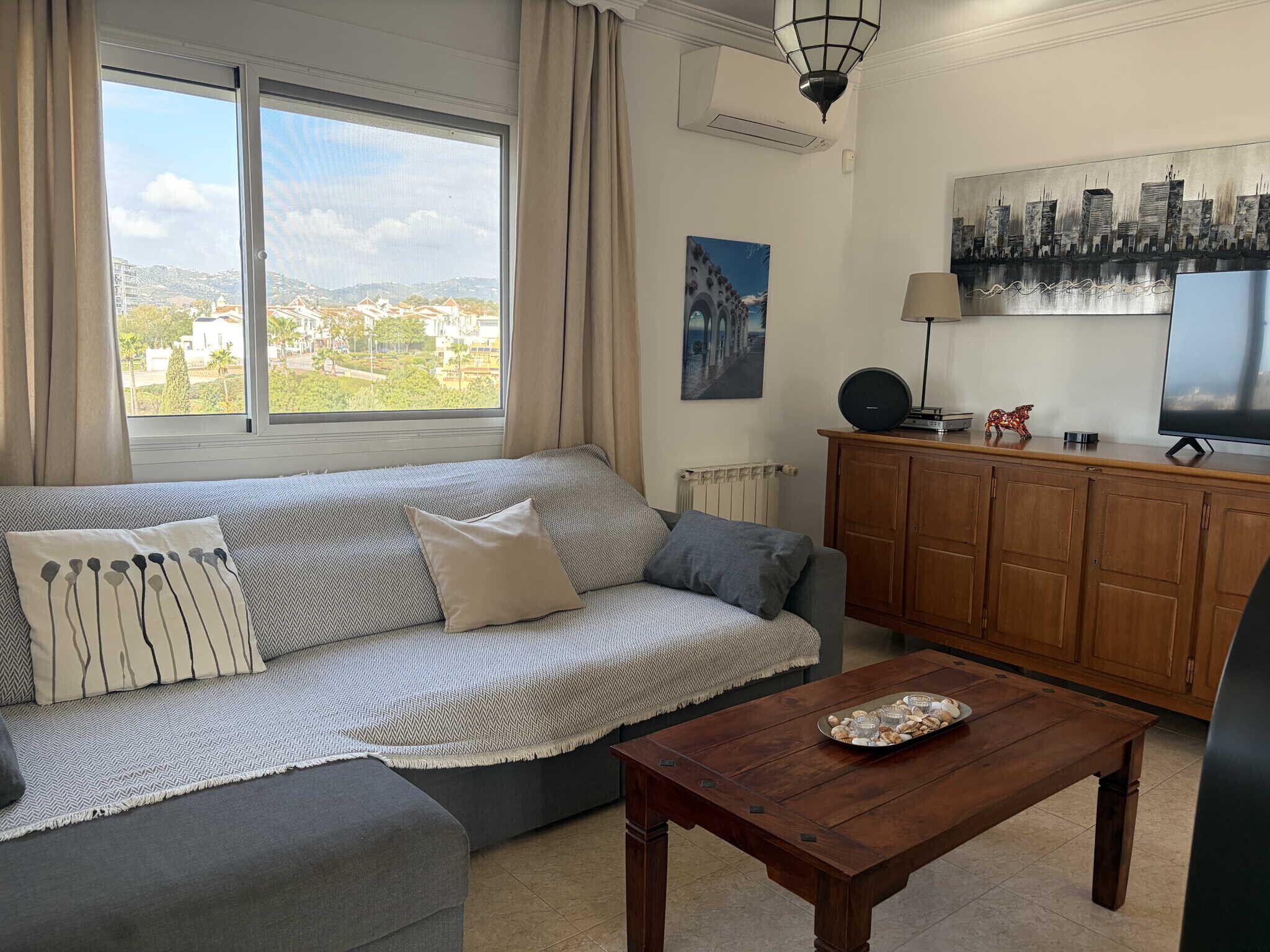 A living room with a sofa, a coffee table, a TV, and a view of a cityscape.