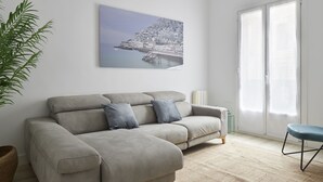 A living room with a grey sofa, a blue chair, a large window, and a framed picture on the wall. - Always Easy I Chillida (San Sebastián/Donostia)