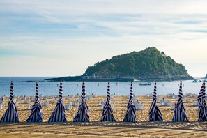 A beach with striped umbrellas and white lounge chairs arranged in rows. - Always Easy I Chillida (San Sebastián/Donostia)