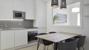 A modern kitchen with white cabinetry, a built-in microwave, an oven, and a dining area with a wooden table and black chairs. - Always Easy I Chillida (San Sebastián/Donostia)