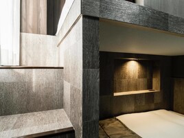 Un dormitorio moderno con una cama litera, una mesita de noche y una lámpara fijada a la pared.