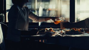 Duas pessoas brindando com bebidas em uma mesa com comida e uma jarra de vidro.