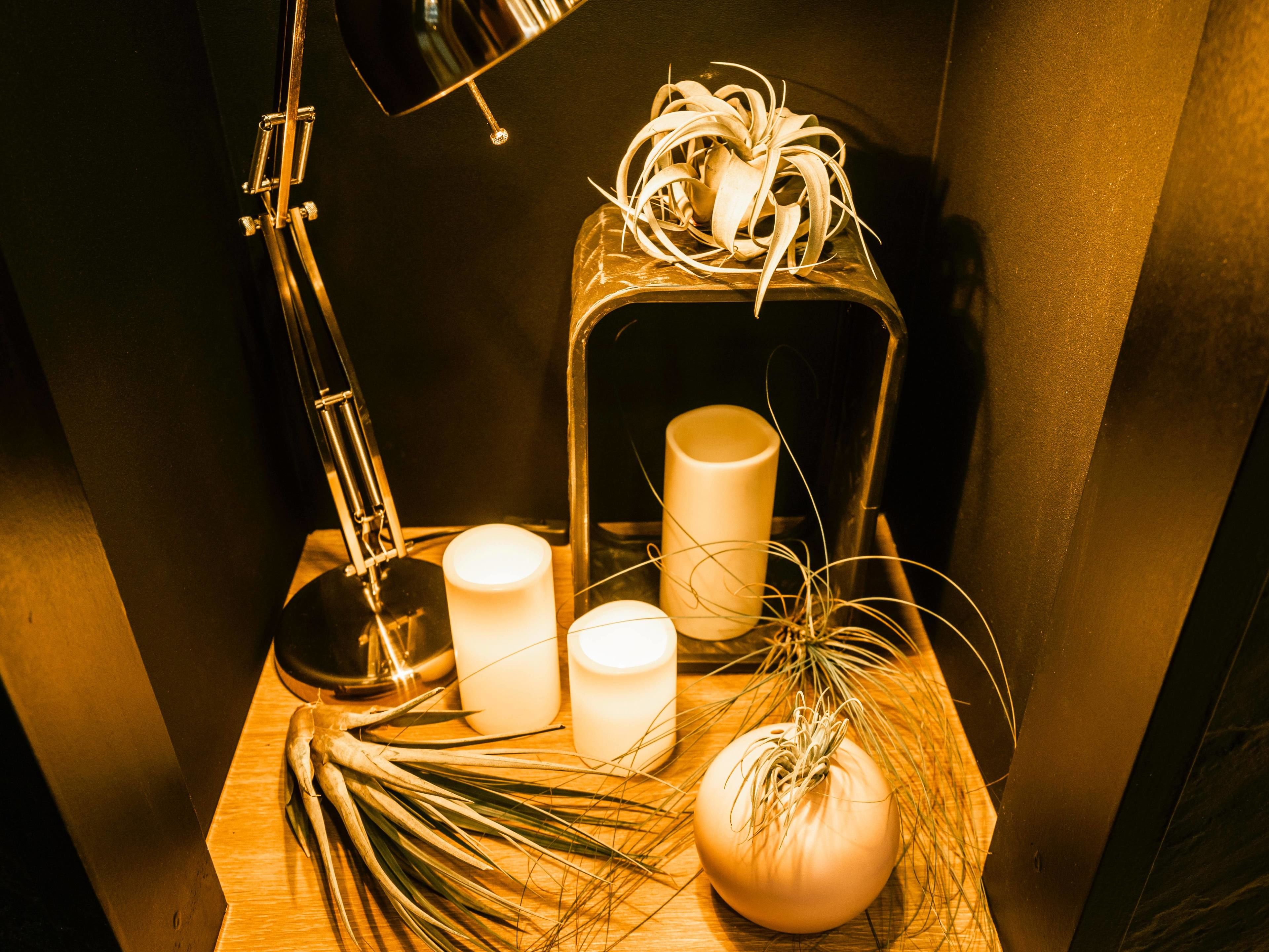 Ein Holztisch mit einer Lampe, Kerzen, einer Zierpflanze und einer Glühbirne.