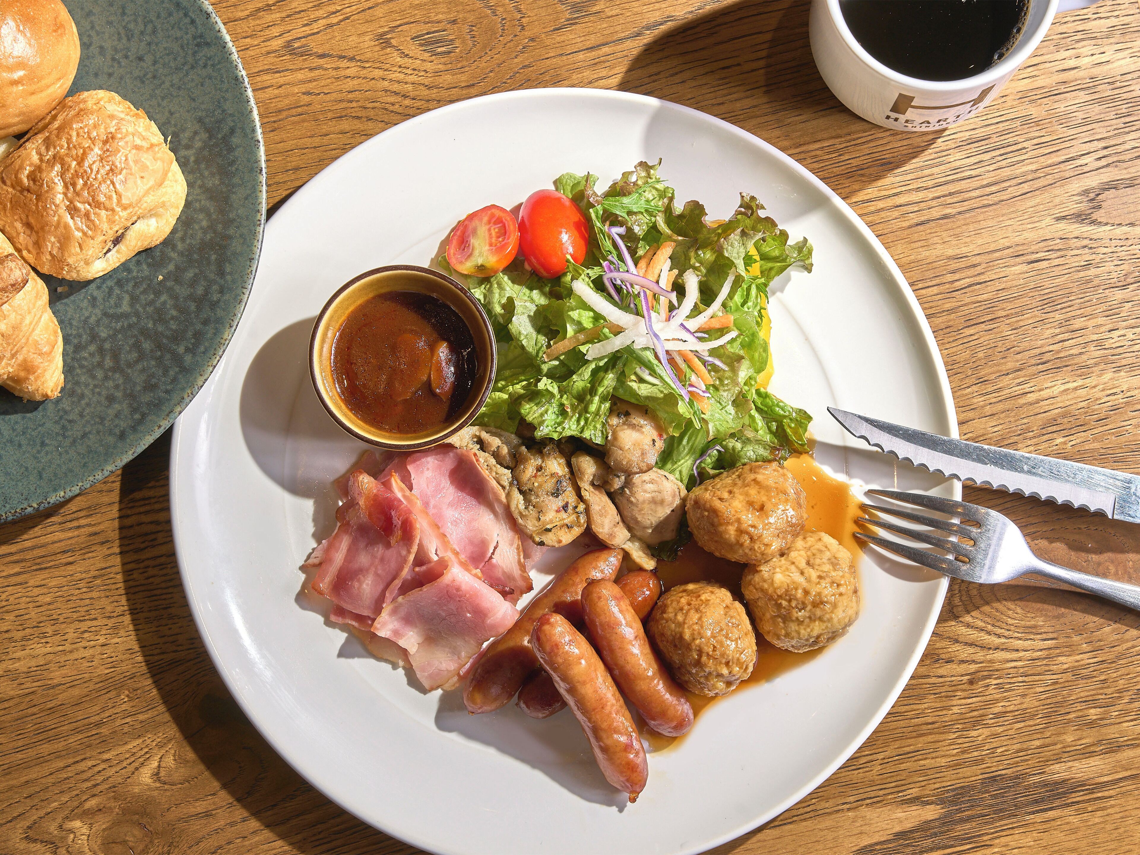 A plate with various foods including sausages, meat, salad, and a small bowl of sauce.