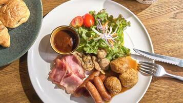 A plate with various foods including sausages, meat, salad, and a small bowl of sauce.