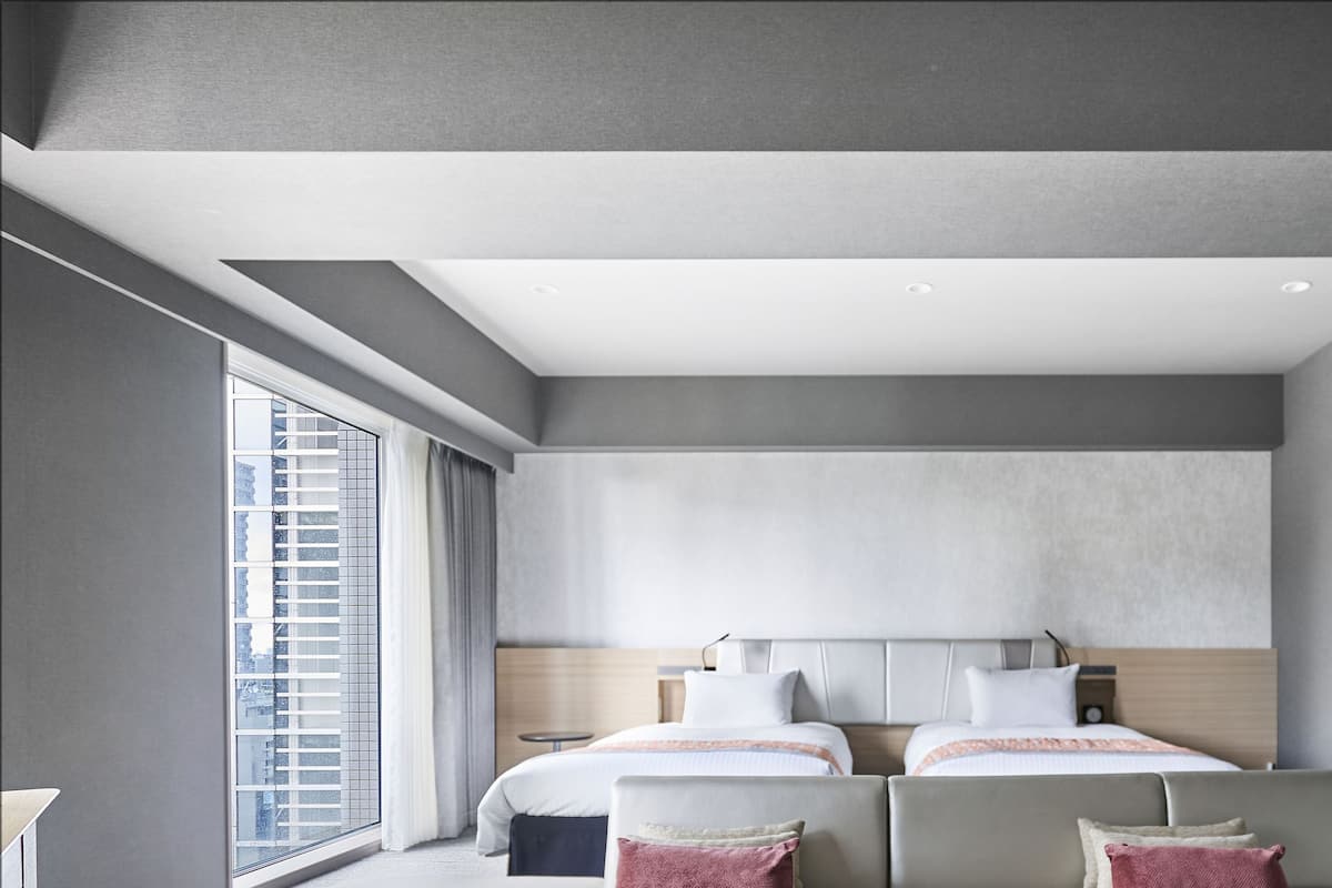 A modern hotel room with two beds, a large window, and a view of the city.