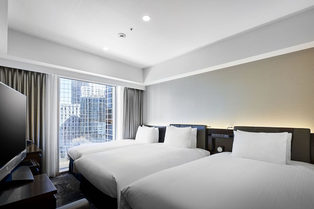 A hotel room with two beds, a flat-screen TV, a desk, and a window with curtains.