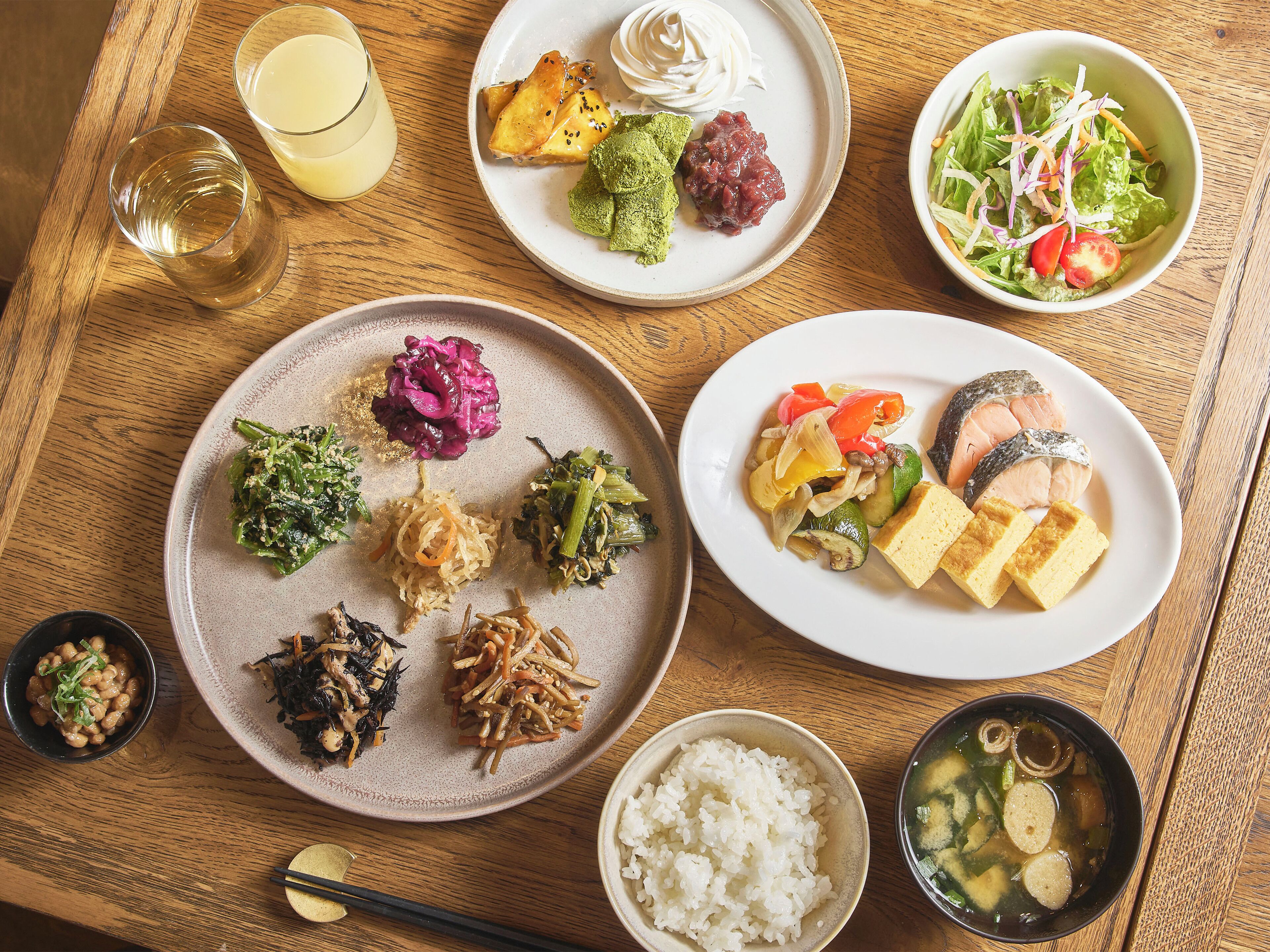 A wooden table with various dishes including sushi, vegetables, and rice.