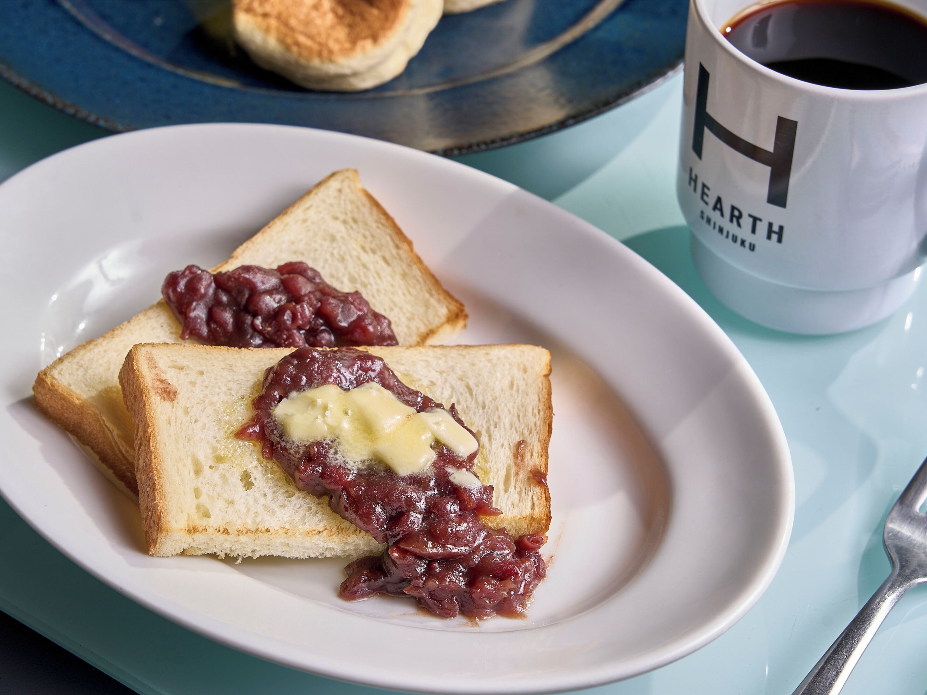 A plate with two slices of toast topped with jam and butter, a cup of coffee, and a biscuit on a blue table.